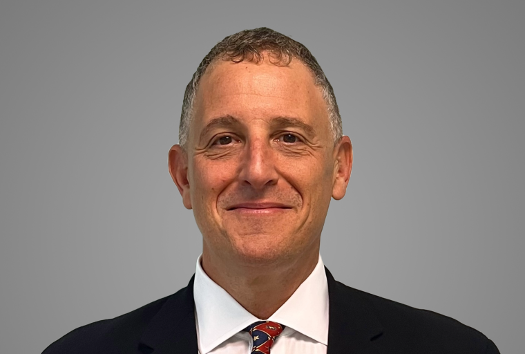 Headshot of Dr. Brian Becker; he's wearing a dark suit, white shirt and red tie and a closed mouth smile.  He has short curly brown hair and a fair complexion.