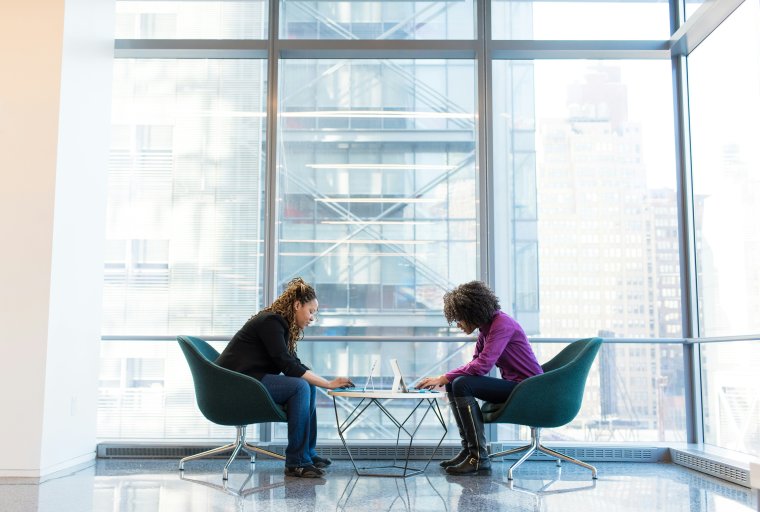 Two individuals sitting on two chairs looking toward each other talking