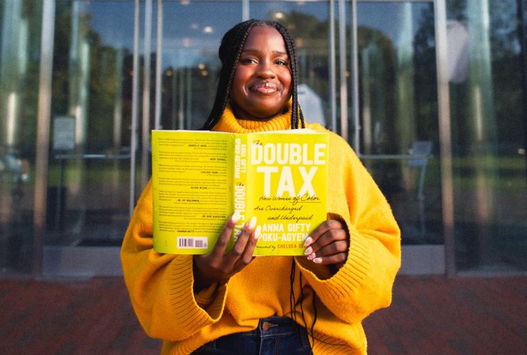 A woman smiles while holding a copy of "The Double Tax" book in her hands.