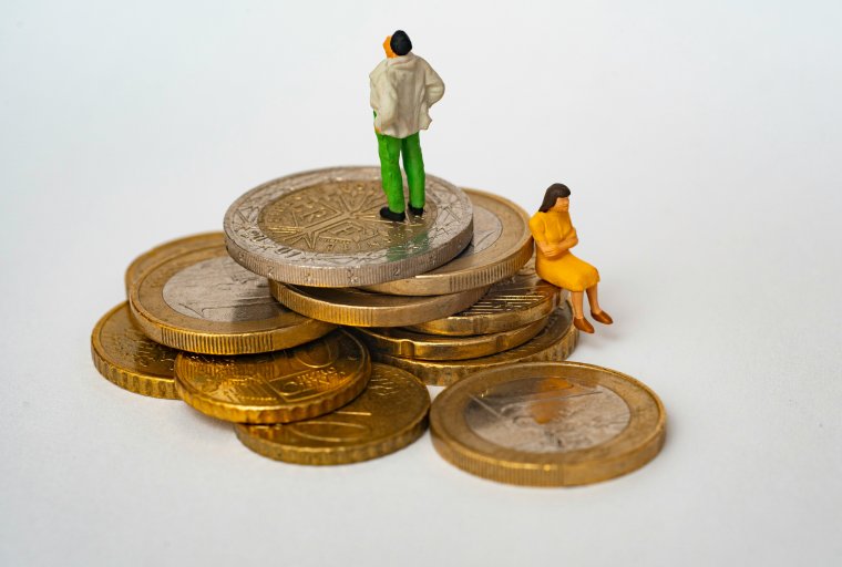 Tiny man and woman standing on top of large stack of coins.