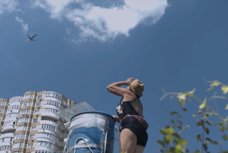 Woman looking up at the sky with a building in the background and a plane flying above.
