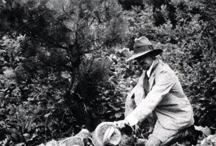 A black and white photograph of James Marshall Plumer outdoors with pottery on the ground Related Links