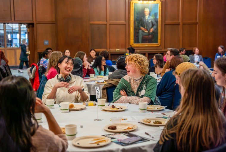 Students sitting at a round table sharing a meal and laughing together.