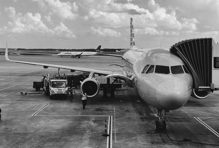 B&W photo of airplane on tarmac with disembarking canopy on right.
