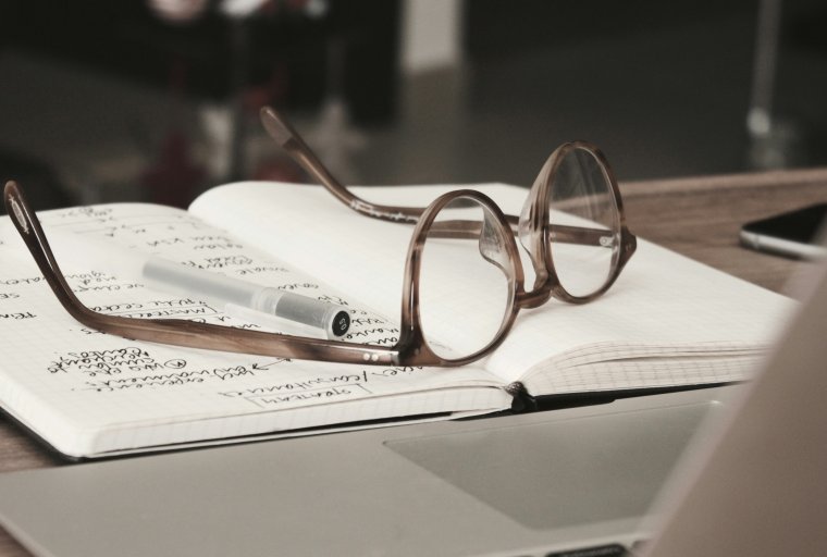 Glasses rest on top of notebook on desk.