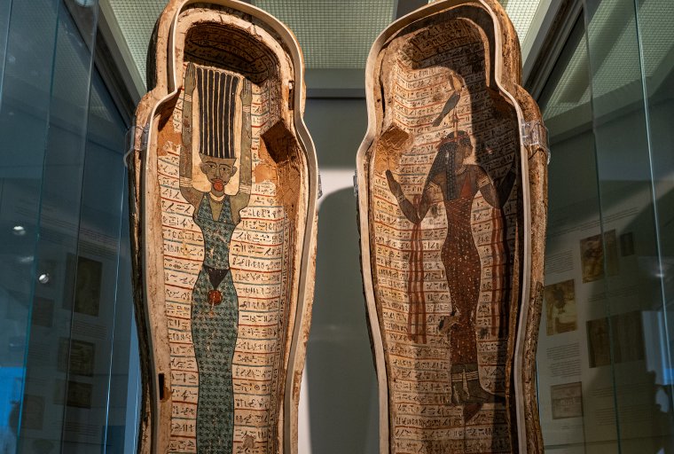 View of the open coffin of Djehutymose, showing painted depictions of the ancient Egyptian goddesses Nut and Amentet standing, surrounded by rows of hieroglyphs. Nut has her hands and hair raised above her head, while Amentet walks in profile with a falcon on her head.
