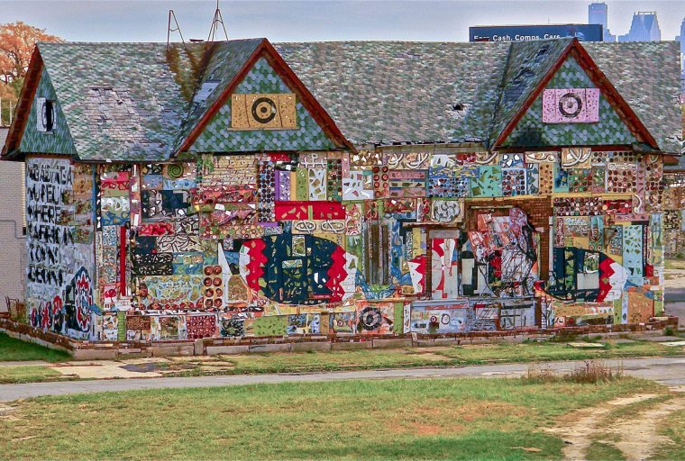 A colorful, two-story building covered in intricate mosaics, beads, vibrant artwork, and painted text.