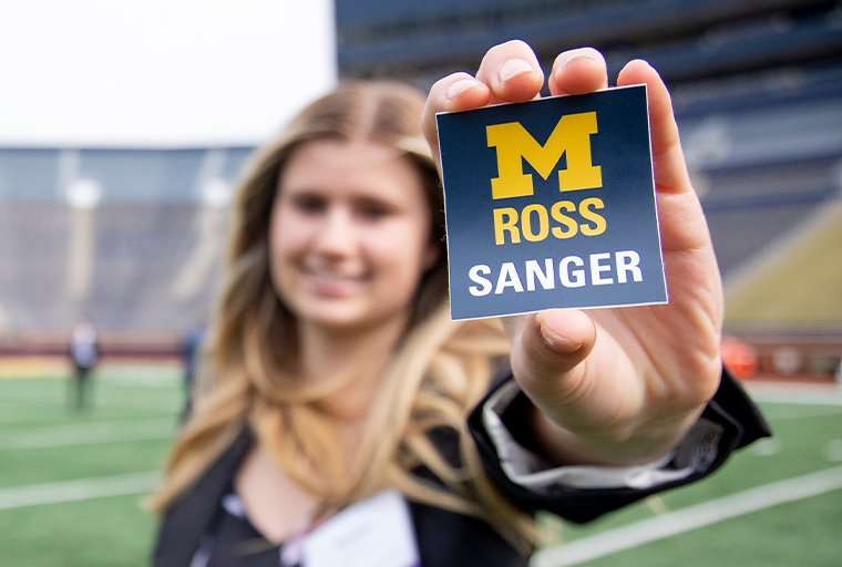 Woman holds sticker w/ Sanger logo in Big House.