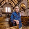 Jim Toy stands at a pew at St. Andrew's Episcopal Church, a light smile lingering on his face. There is a glint in his eyes, the sleeves of his blue plaid shirt rolled up.
