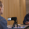 Two students sit across from each other, engaged in conversation, while one films the interview