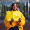 A woman smiles while holding a copy of "The Double Tax" book in her hands.
