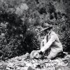 A black and white photograph of James Marshall Plumer outdoors with pottery on the ground Related Links