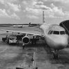 B&W photo of airplane on tarmac with disembarking canopy on right.