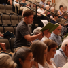 Male singer stands in tiered seating holding music binder.