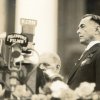 Vintage photo of a man in a suit (Manuel Quezon) standing near a bank of microphones at an outdoor speech.