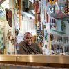 Olayami Dabls smiling behind a counter inside the museum filled with hanging beads, masks, and artwork.