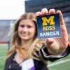 Woman holds sticker w/ Sanger logo in Big House.