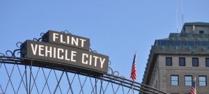 A picture of a metal sign against a clear sky that reads "Flint: Vehicle City."