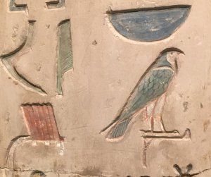 Painted hieroglyphs on the false door of an Egyptian official nicknamed Pepy Nefer. The hieroglyphs visible are carved into the stone and look like a hawk, a bowl, a feather, and a sickle.