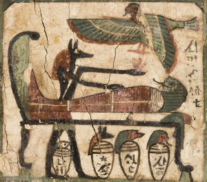 This is one of the many scenes on the coffin of the ancient Egyptian priest Djehutymose. In this scene, the jackal-headed god Anubis stands at the foot of a bed with his arms outstretched. The coffin of Djehutymose lies on the bed while overhead a ba bird flies holding the heart of Djehutymose.