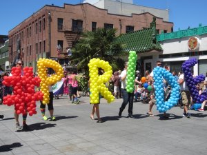A group of people holding up rainbow colored balloons that spell out "#PRIDE"