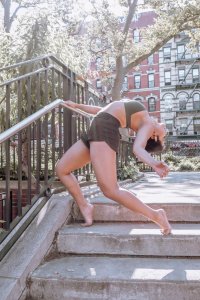 Dancer poses in a backbend on the concrete steps of a sunny park.