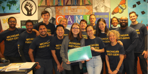 A row of students and staff in the Office of Academic Multicultural Initiatives wearing t-shirts that read Michigan First Gens.