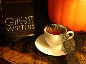 A spider weaves a web over a teacup near a pumpkin and a copy of Ghost Writers