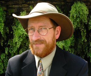 White man with full beard wearing a brown hat, suit and tie
