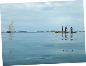 A sailboat and a fishing boat on the water, people dropping nets
