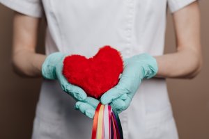 Gloved hands holding felt heart with colorful strings at the end