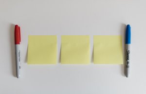 three yellow sticky notes laying in between red and blue sharpie markers