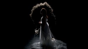 A silhouette of a women in a long white dress standing against a dark, black back ground.