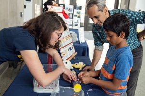 U-M scientist explains her research to a boy and man.