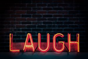 Neon light sign reading "Laugh" in red letters in front of a brick wall | Instagram: @timmossholder