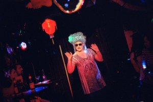 A drag queen in sunglasses dancing in a nightclub.