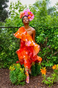 A woman in an orange dress stands in a garden.