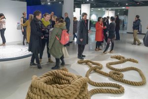 People at a Stamps Gallery exhibition reception gather near a large coil of rope in the foreground