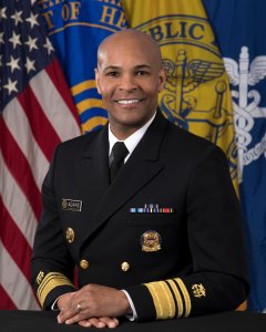 Doctor Jerome Adams wearing his Public Health Corp uniform adorned with medals sitting in front of the American flag.