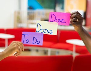 two hands holding up notes saying "To Do", "Doing", and "Done"