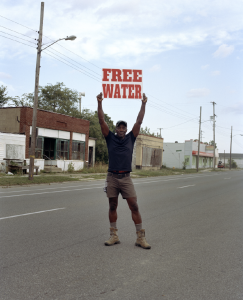 LaToya Ruby Frazier, &quot;Moses West Holding a “Free Water” Sign on North Saginaw Street Between East Marengo Avenue and East Pulaski Avenue, Flint, Michigan,&quot; 2019/2020. Copyright LaToya Ruby Frazier. Courtesy of the artist and Gladstone Gallery.