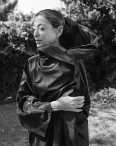 a woman stands with her eyes closed with a dark satin fabric rapid around her.