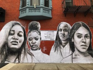 large mural on a red brick wall of 4 black women in black and white