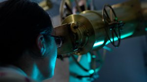 Image of a man with glasses looking into a telescope.