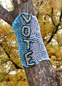 knitted tree warmer with word 'vote' wrapped around tree in forest of fall leaves