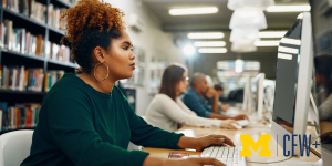 Black woman with hair up sitting at a computer in a library