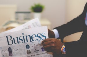 Photo of a person in a suit holding a paper with the title 'business" at the top.