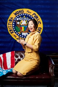 Kristina Wong poses on a leather sofa in front of a homemade seal of office