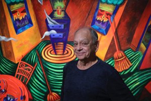 Cheech Marin poses in front of a brightly colored painting by Patssi Valdez