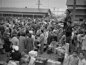 A circa-1942 black-and-white news photograph depicting hundreds of Americans of Japanese descent -- men, women, and children -- amassed at a train depot awaiting transport to internment camps. [Credit: Seattle Post-Intelligencer Collection]